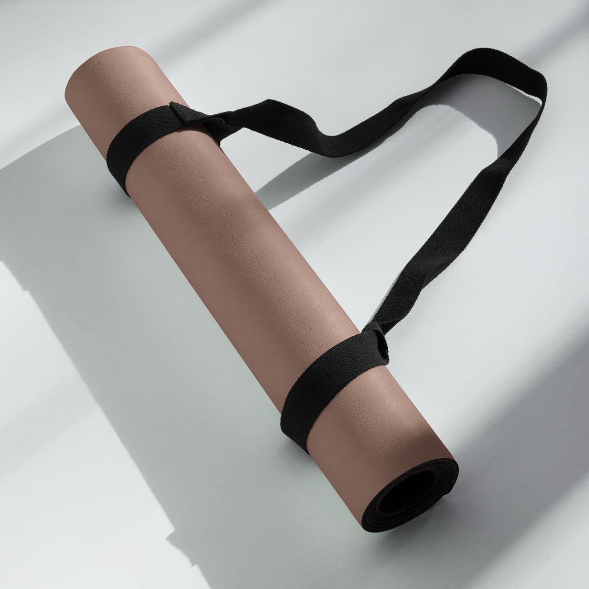 Chocolate yoga mat with black carrying strap looped around it