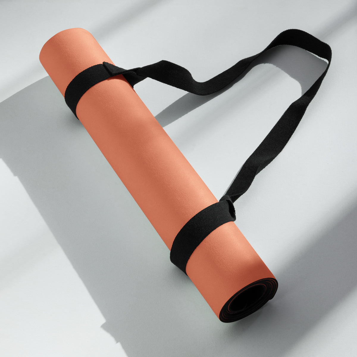 Rolled orange yoga mat secured with a black strap and end caps.