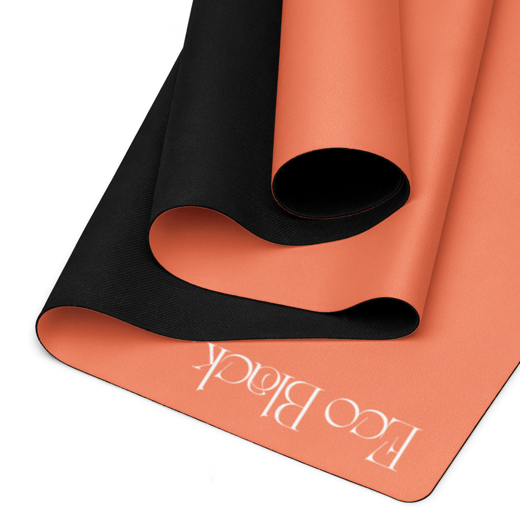 Orange yoga mat with black textured traction underside and embossed brand text near edge.
