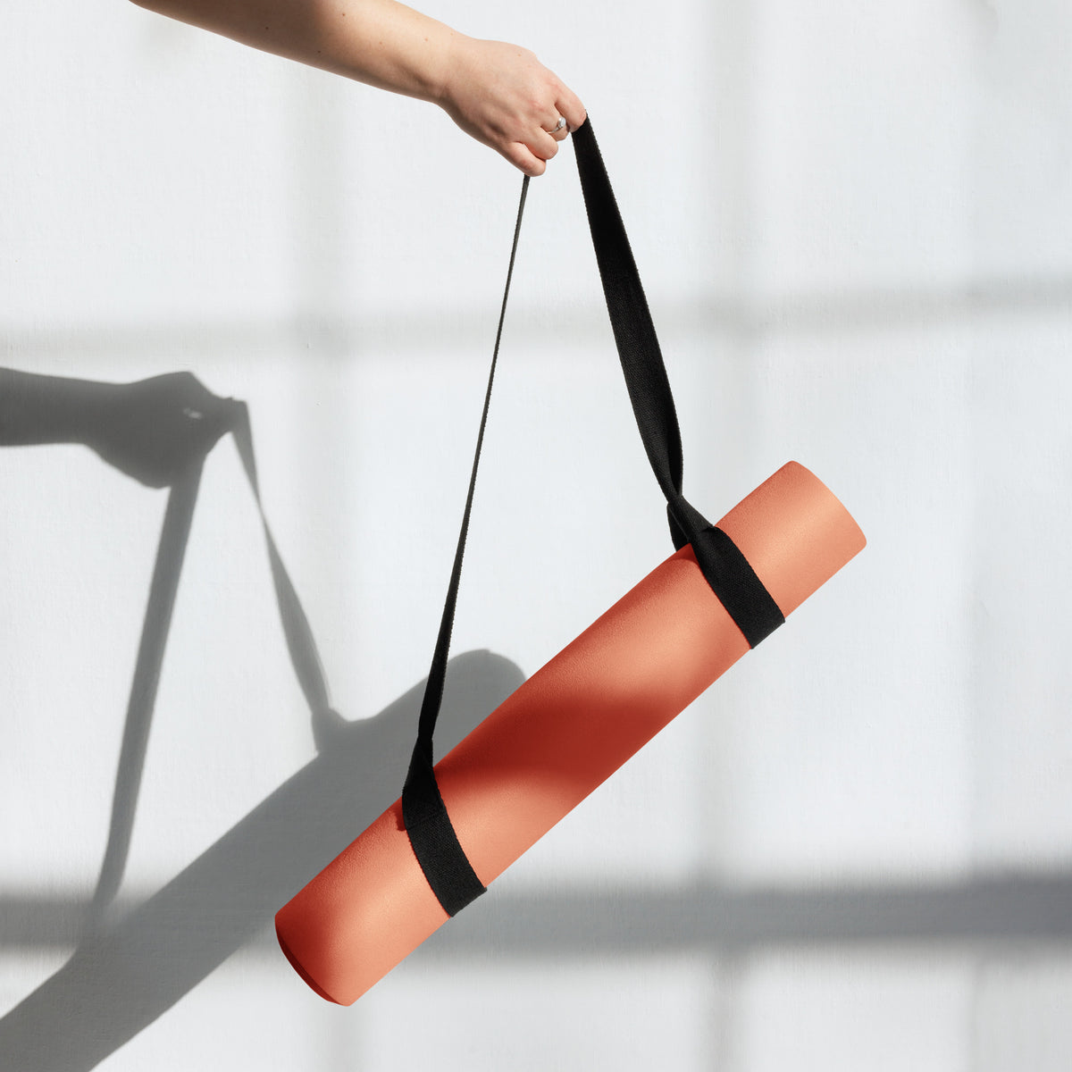 Orange yoga mat rolled and carried with a black strap and end rolled section.
