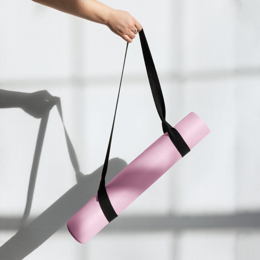 Pink yoga mat carried by a black strap, held upright in one hand