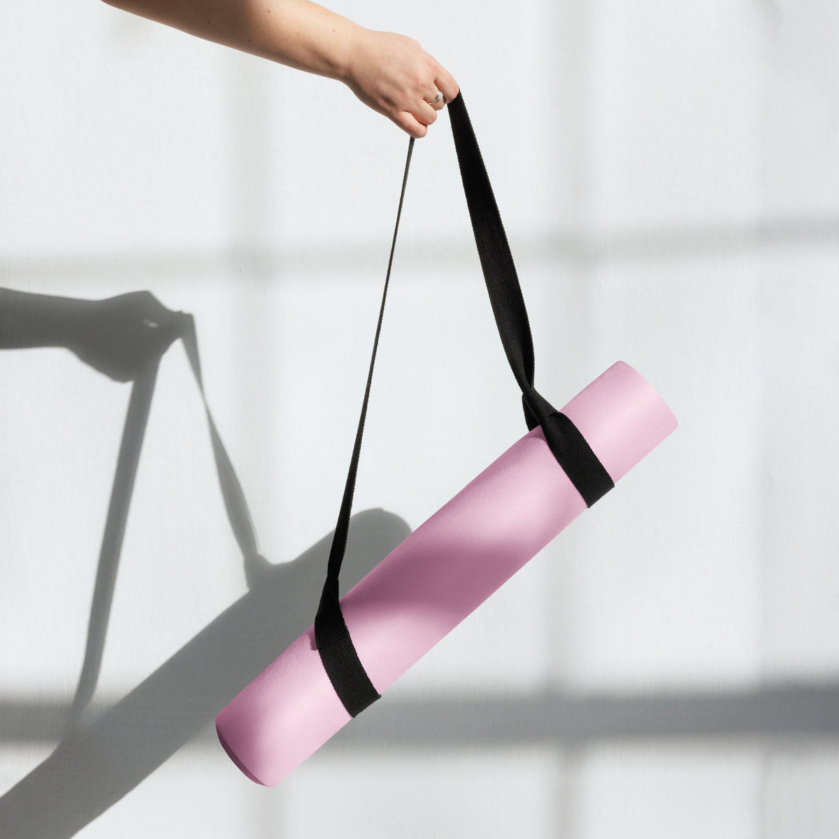 Pink yoga mat carried by a black strap, held upright in one hand