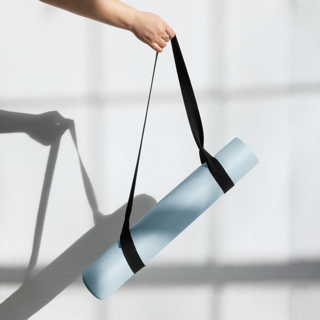Natural rubber yoga mat in powder blue held with black carry strap.