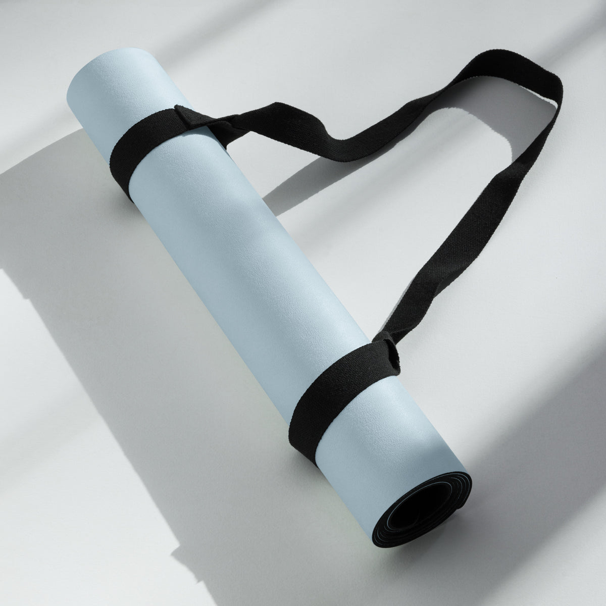Powder blue yoga mat rolled with black carry straps, overhead view.