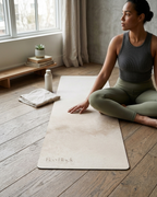Light beige yoga mat on wooden floor during seated stretch pose